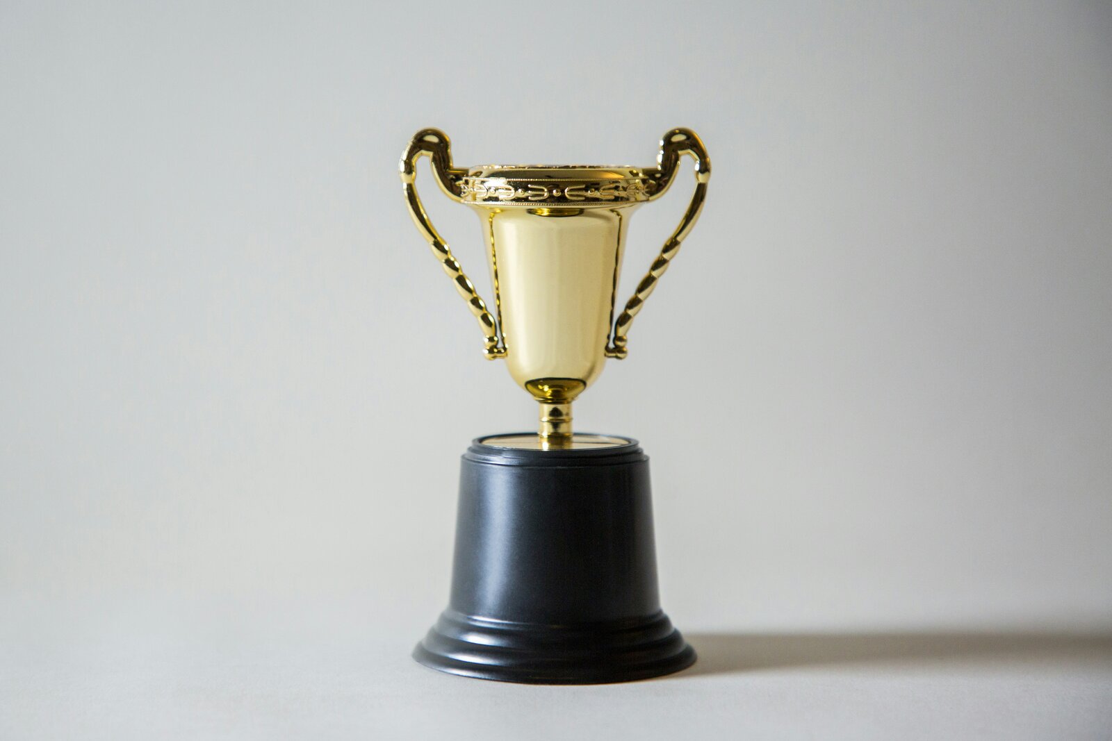 A small gold trophy cup with a black base, on a plain gray background